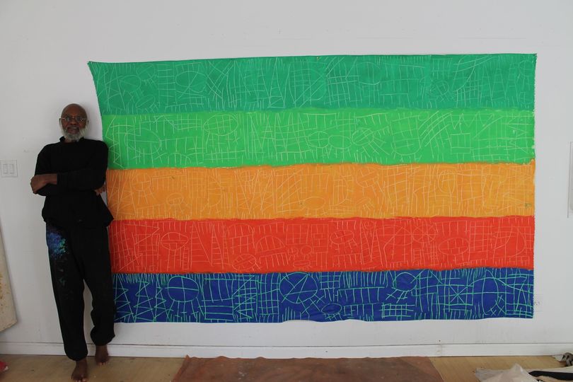 a picture showing moyo okediji standing next to his artwork