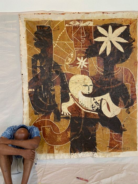a picture showing moyo okediji sitting with his head hidden between his thighs next to his artwork