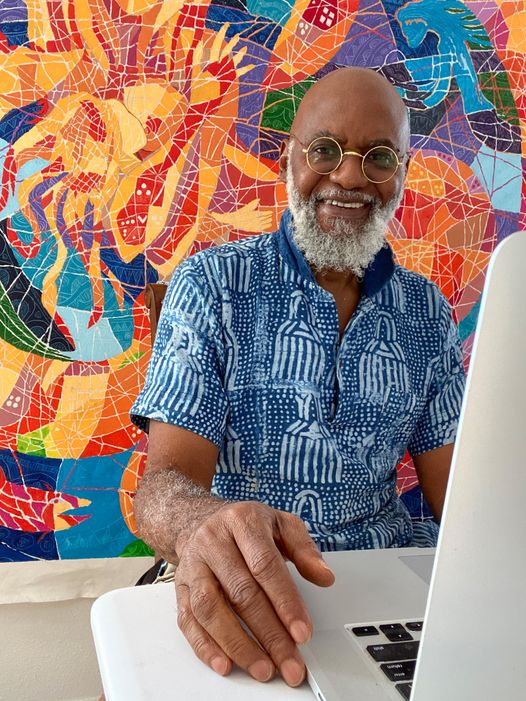 a picture showing moyo okediji sitting in front front of his artwork with a laptop in front of him.