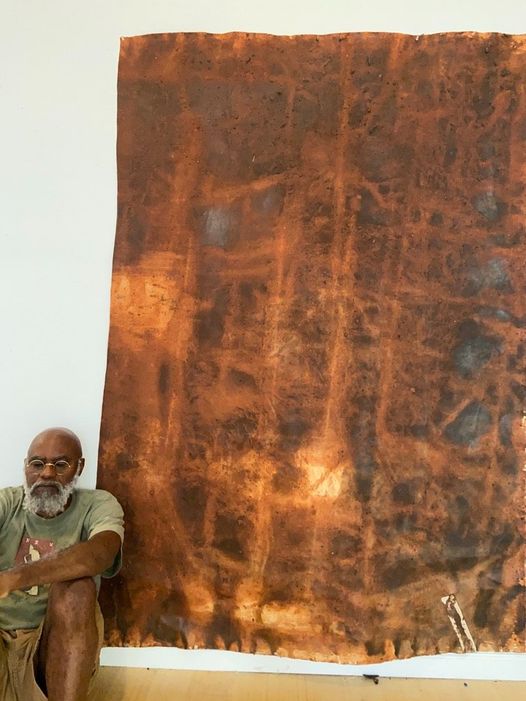 a picture showing moyo okediji sitting next to his artwork
