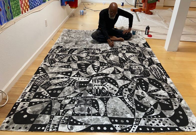 A picture of Moyo Okediji sitting in front of his artwork