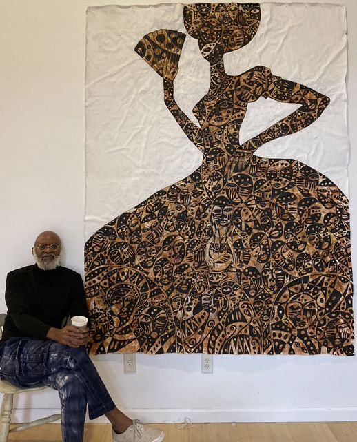 a picture showing moyo okediji sitting next to his artwork