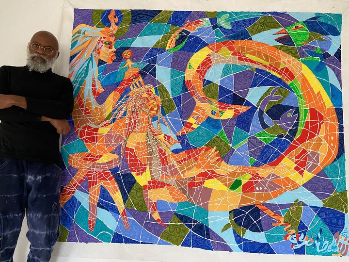 a picture showing moyo okediji standing next to his artwork